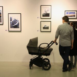 couple with baby standing in front of wall of framed photos