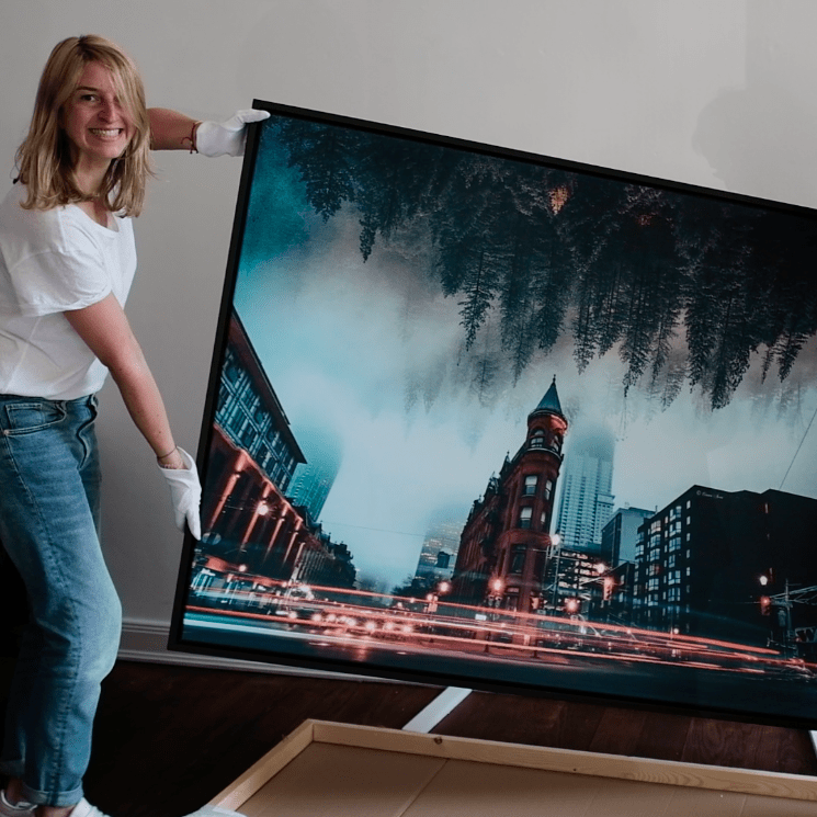 anna stoffel smiling and holding a framed canva showing a building and a forest in the sky