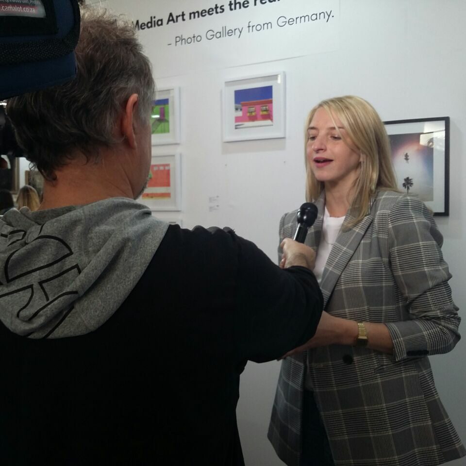 gallery owner anna stoffel giving an interview in front of gallery artworks